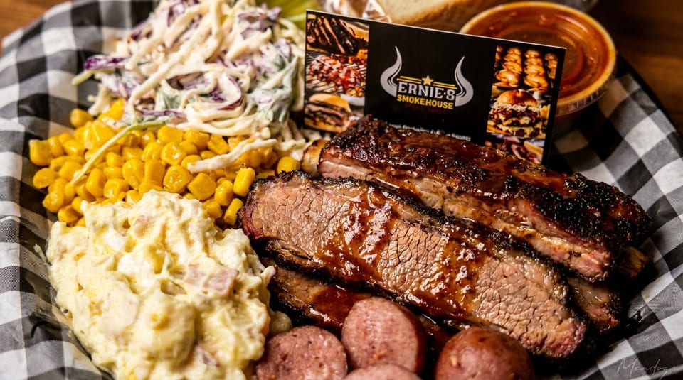 Ernie's Smokehouse platter with ribs, brisket, sausage, coleslaw, corn, and potato salad.