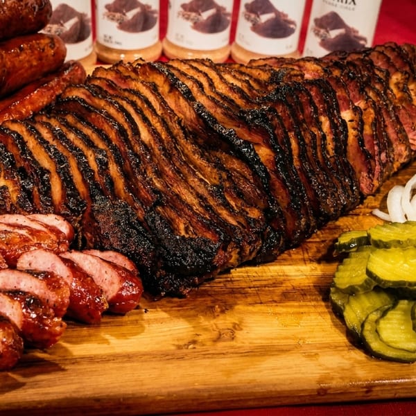 Smoked brisket, sausages, sliced onions, and pickles on a wooden cutting board.